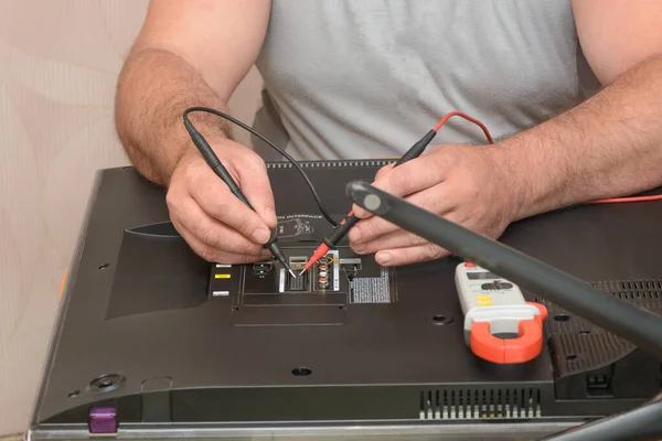 Diagnostics and repair of LCD TV. Engineer takes sample with multimeter on back of large monitor.