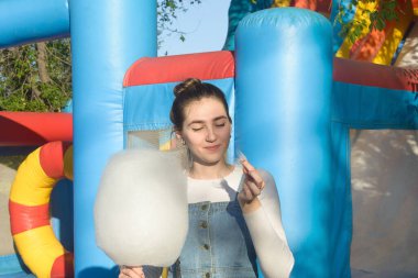 Parkta trambolinin yanında pamuk şekerli genç ve mutlu bir kadın. Mutlu hafta sonu konsepti.