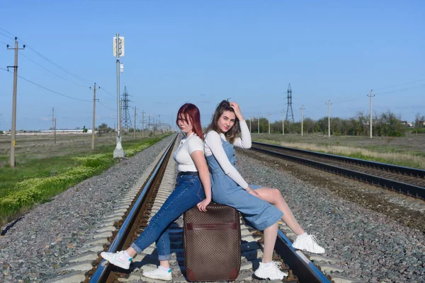 两个年轻的妇女带着手提箱坐在铁路上 旅行概念 — 图库照片