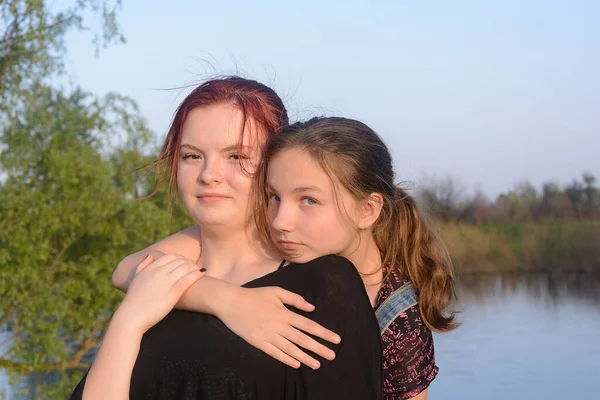 Two teenage sisters hug on the river bank.