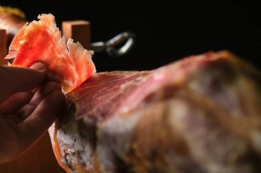 Dry Spanish ham, Jamon Serrano, Italian Prosciutto Crudo or Parma ham, whole leg on black background.Slice of ham in a man's hand.