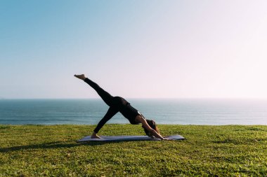 Öğretmen denizin önündeki çimenlikte yoga yapıyor. Boşluğu kopyala