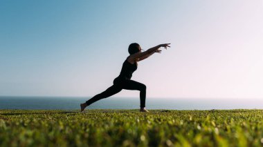 Arkadaki gökyüzünde yoga yapan güzel bir kadının silueti. Boşluğu kopyala