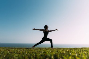 Çimlerin üzerinde yoga yapan genç bir kadın kollarını açmış ve darmadağın olmuş.