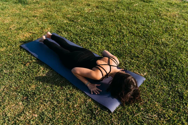 Paspasında uzanmış, çimlerin üzerinde yoga yapan bir kadın.