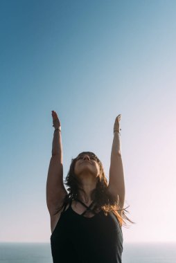 Siyahlar giymiş, kollarını gökyüzüne kaldıran zayıf bir kadının dikey görüntüsü. Yoga konsepti. Boşluğu kopyala