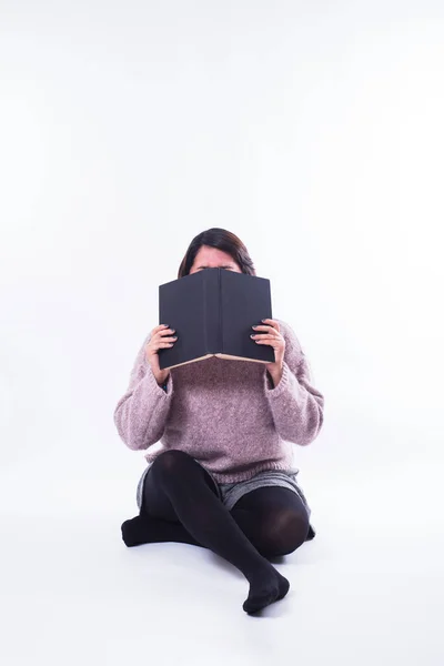 Woman covers her face with a blue book, she is sitting. Copy space