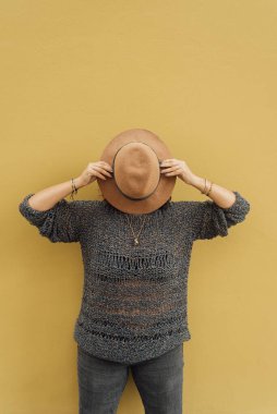 Kadın yüzünü sarı bir duvara yasladığı bir şapkayla kapatıyor. Tuhaf bir şehir imajı. Dikey resim kopyalama alanı