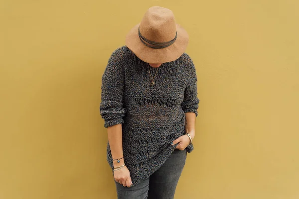 彼女のポケットに片手で見下ろして帽子をかぶった女性と マスタードイエローの壁にもたれて彼女の服を引っ張る他の人 都市型ファッションの概念 スペースのコピー — ストック写真