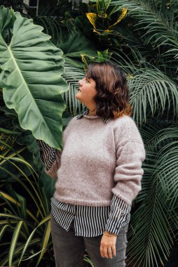 vertical image of woman looking sideways at an elephant ear leaf on a foliage