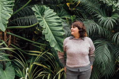 woman with hands in back pockets with foliage background copy space