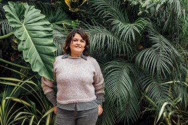 girl with hands in back pocket and looks at camera with copy space foliage background