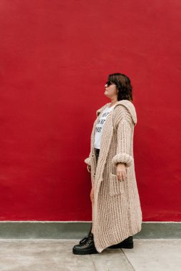 Sol taraftaki uzun boylu kadın, uzun bir süveter giyiyor, koyu gözlükler, uzun süveter, kırmızı arka planda siyah çizmeler. Boşluğu kopyala