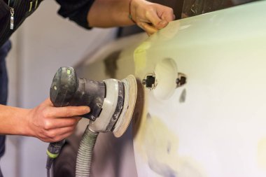 Araba tamirhanesinde araba cilalayan bir adamın elinde öğütücü..