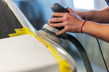 Araba tamirhanesinde araba cilalayan bir adamın elinde öğütücü..