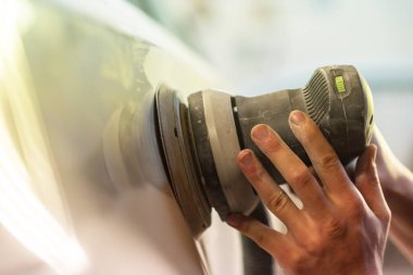 Araba tamirhanesinde araba cilalayan bir adamın elinde öğütücü..