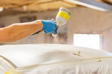 Özel garajda beyaz bir araba boyuyor, kostüm ve koruyucu giysiler giyiyor..