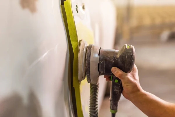 Grinder in the hands of a man who sharpen a car varnish in the car shop.