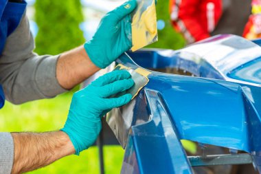 Araç atölyesindeki bir kazada vücudun bir kısmına hasar verdikten sonra ön ateşleme uygulamadan önce bir servis teknisyeninin Emery göndericisini kullanarak araba unsurunu boyama hazırlığı.