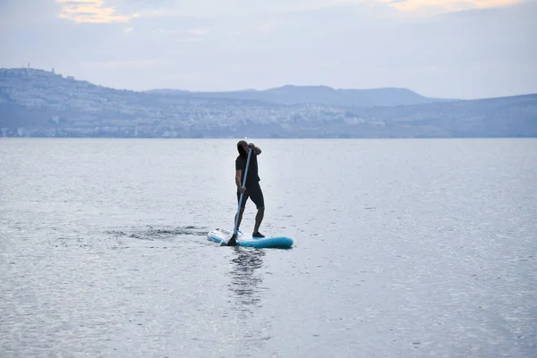 Man sail on a SUP board in a large lake during sunrise. Stand up paddle boarding - active recreation in nature.