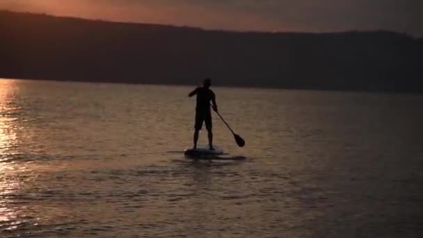 L'uomo naviga su una tavola SUP in un grande lago durante l'alba. Stand up paddle imbarco ricreazione attiva in natura — Video Stock