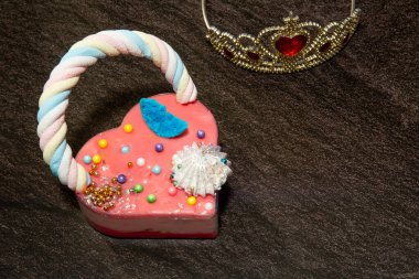  Pembe kalp şeklinde pasta ve siyah mermer arka planda bir prensesin tacı ve bir sürü küçük renkli şekerler. Sevgililer Günü. Aşk hakkında. Boşluğu kopyala