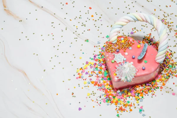 Pink heart shape cake on a white marble background with a lot of small colorful candies . Valentine day. About love. copy space — Stock Photo, Image