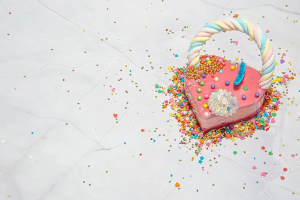 Pastel en forma de corazón rosa sobre un fondo de mármol blanco con una gran cantidad de pequeños caramelos de colores. San Valentín. Sobre el amor. espacio de copia —  Fotos de Stock