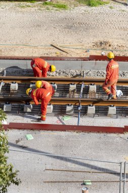 Tel Aviv, İsrail - 20 Mayıs 2021: Turuncu tulumlu inşaat işçileri. Hafif raylar. Mavi yakalı işçi. İşbirliği ekip çalışmasını kabul et. Kamyonlar, beton karıştırıcı, buldozer.. 
