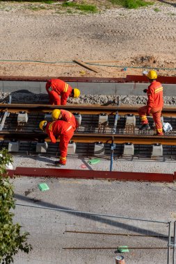 Tel Aviv, İsrail - 20 Mayıs 2021: Turuncu tulumlu inşaat işçileri. Hafif raylar. Mavi yakalı işçi. İşbirliği ekip çalışmasını kabul et. Kamyonlar, beton karıştırıcı, buldozer.. 