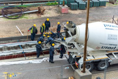 Tel Aviv, İsrail - 20 Mayıs 2021: Yağmurda çalışan inşaat işçileri. Hafif raylar. Mavi yakalı işçi. İşbirliği ekip çalışmasını kabul et. Kamyonlar, beton karıştırıcı, buldozer.