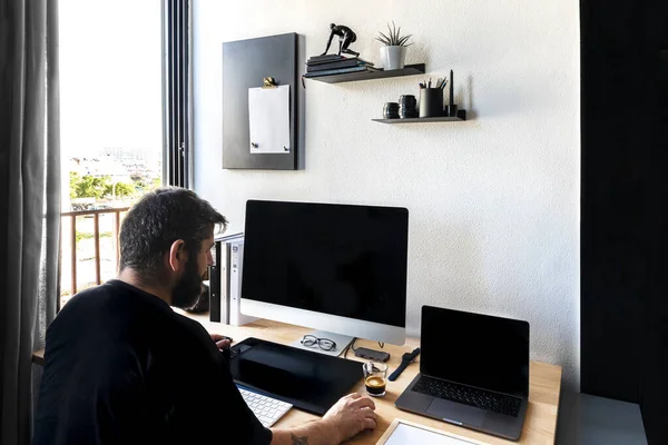 Millennial Caucasian zitten aan een bureau op kantoor te kijken naar een computerscherm werken met papieren documenten. Ernstige jongeman werkt op de computer online op de werkplek, raadpleeg klant of klant. — Stockfoto