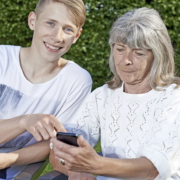 Young man teaching a senior woman to use a smartphone — Stock Photo, Image