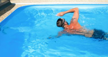 Genç bir adam ev havuzunda antrenman yapıyor. Sporcu karşı akımda yüzer. Sağlıklı bir yaşam tarzı olarak spor eğitimi.