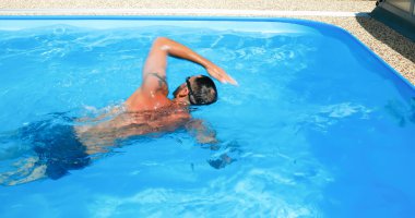 Genç bir adam ev havuzunda antrenman yapıyor. Sporcu karşı akımda yüzer. Sağlıklı bir yaşam tarzı olarak spor eğitimi.