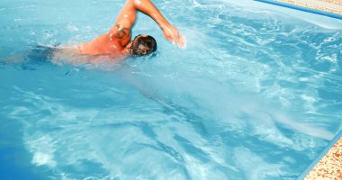 Genç bir adam ev havuzunda antrenman yapıyor. Sporcu karşı akımda yüzer. Sağlıklı bir yaşam tarzı olarak spor eğitimi.