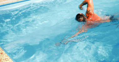 Genç bir adam ev havuzunda antrenman yapıyor. Sporcu karşı akımda yüzer. Sağlıklı bir yaşam tarzı olarak spor eğitimi.