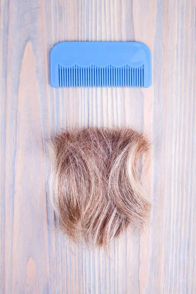 Blond hair lock, blue plastic comb light wooden background close up, cut off natural blonde hair curl on bright wood, hair brush, hair snip design, haircut, hairstyle, hairdo, coiffure, barber concept