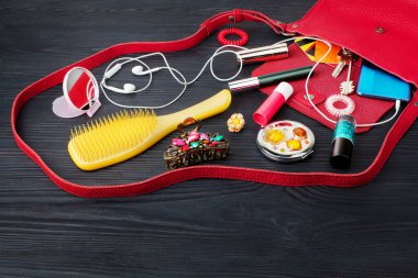 Açık kırmızı deri çanta siyah ahşap arka plan üst görünüm, makyaj kozmetik, saç fırçası, toka, akıllı telefon, kulaklık, anahtar, kredi kartı, kadın aksesuar konsepti, moda kızı çantası