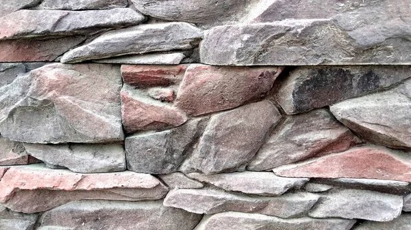 現代のレンガの壁は さまざまな形と大きさの不均一な鋭利な石で構成され ほこりっぽい赤灰色で構成されています — ストック写真