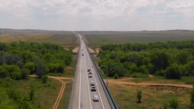 Köprünün Ural nehri üzerindeki hava manzarası, yukarıdan yaz manzarası ve karayolu ulaşımı. Köprünün etrafında bir nehir ve bir sürü yeşil ağaç var.