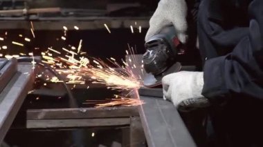 Ustanın elleri metali öğütücüyle öğütüyor, metalden parlak parıltılar çıkıyor. Yakından çekilen bir atölyede metal bir çerçevenin dikişlerini öğütüyor. Yavaş çekim
