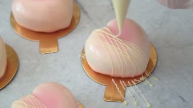 Profesyonel pasta şefi, lezzetli bir tatlıyı hamur torbasıyla süslüyor, mutfak masasına kalp şeklinde beyaz pasta döküyor..