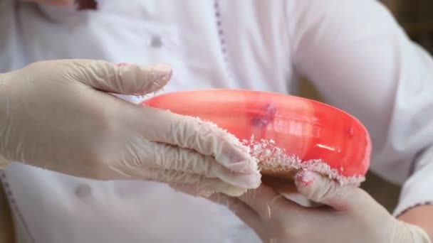 Zbliżenie, cukiernik kucharz strony dekoracje z białego wiórów kokosowych dno ciasto okrągły kształt, pokryte czerwoną glazurą, proces podejmowania pyszne słodkie deser — Wideo stockowe