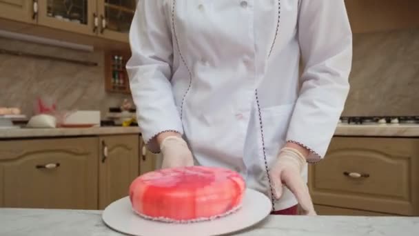 Eine Konditorin zeigt in Großaufnahme, wie süße, köstliche Kuchen mit roter Glasur in der Küche zubereitet werden. Chef zeigt das fertige Dessert, lächelt — Stockvideo