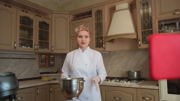 부엌에서 요리하는 여자는 반죽 기계에 재료를 섞고, 요리 방법을 말하고, 그녀의 요리 블로그를 위한 스마트폰에 비디오를 찍는다. — 비디오