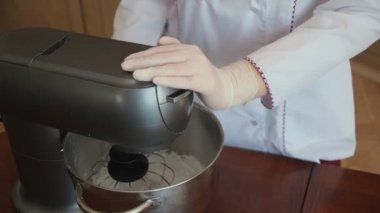 Hamur işi kadın, gülümsüyor, mutfakta, elektrikli mikserin içindeki malzemeleri çırpıyor, çırpıcıyı kaldırıyor ve lezzetli bir tatlı hazırlamak için beyaz, kalın bir krema gösteriyor.