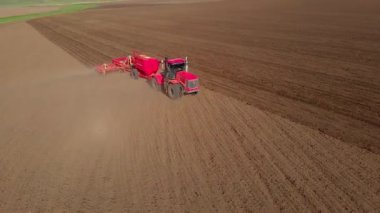 Tarlada modern bir tarımsal kırmızı traktör zemini tırmıklarla donatıyor, düz bir yönde hareket ediyor, tohum ekmeden önce toprağı kontrol ediyor, bir hava aracından görüş sağlıyor.