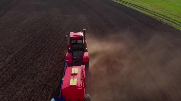 Lavori agricoli, trattore rosso, aratro con rastrelli solca il campo, aratura il terreno fertile, raccoglie una colonna di polvere, prepara il terreno per piantare una nuova coltura, abbagliamento dei raggi solari, vista dall'alto — Video Stock