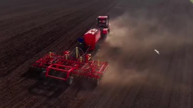 Tarım sektöründe, modern enerji zengini kırmızı traktör toprağı sürerek toprağı sürüyor, toprağı yeni bir ekin için hazırlıyor, toz sütunu, güneş ışınlarının parlaklığı, insansız hava aracının dairesel hareket etmesi...